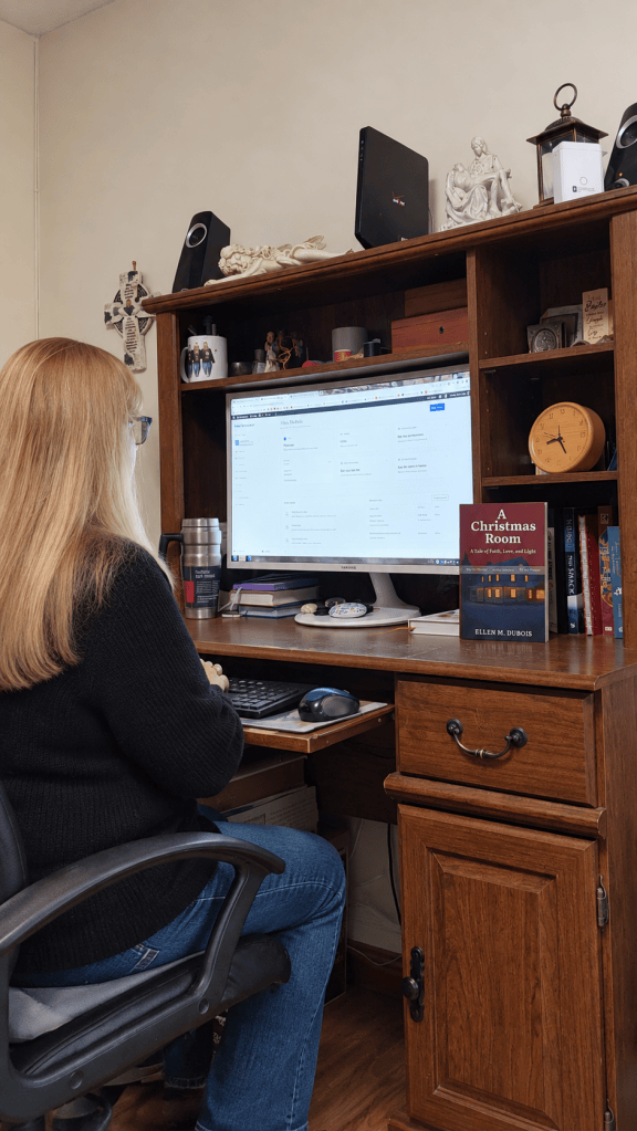 Christian author Ellen M. DuBois at her writing desk, with her novel A Christmas Room displayed beside her computer.